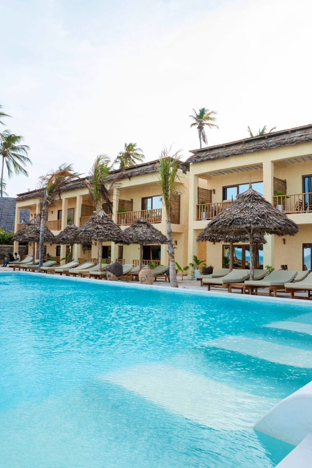 Luxury Zanzibar beachfront resort with infinity pool, thatched palapa sunbeds and palm trees at sunrise.