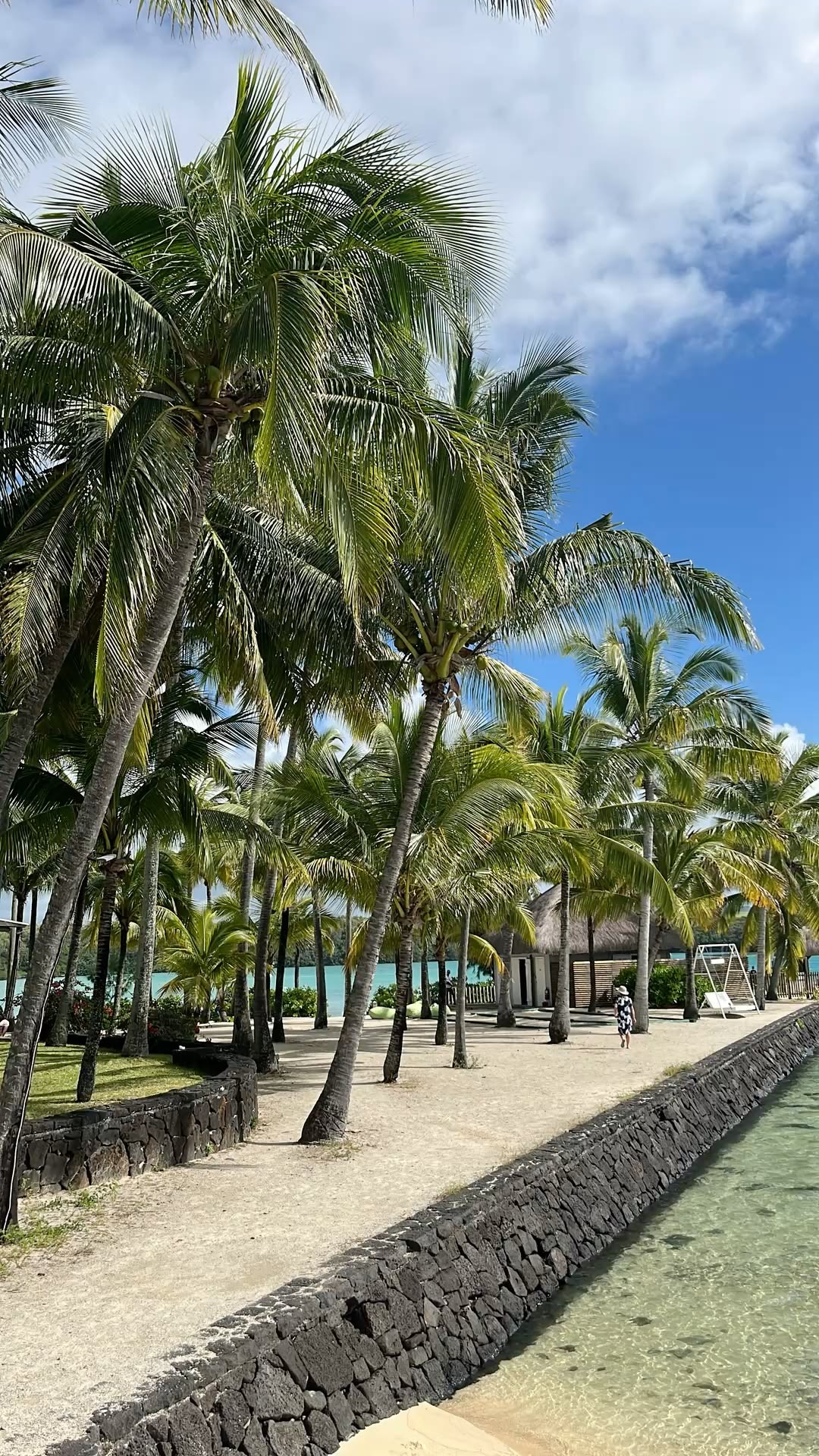 Coconut palms lining a sandy resort promenade beside a clear turquoise lagoon channel on the Indian Ocean coast.