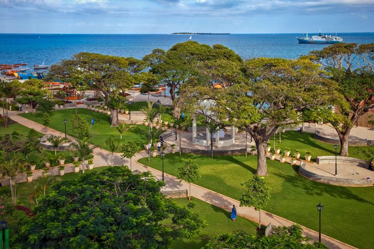 Sweeping aerial view of Forodhani Gardens, Stone Town seafront promenade and dhows on the Indian Ocean at golden hour.