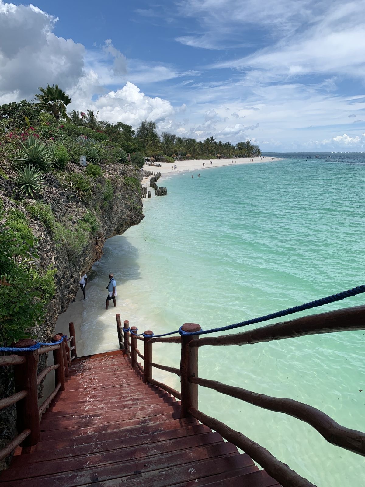Wooden cliffside staircase leading down to the powder-white sands and emerald shallows of Kendwa Beach, Zanzibar.